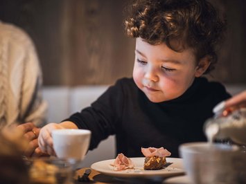 Bontà locali e di stagione al Klessler’s Bambino che fa colazione con pane, prosciutto e una tazza in mano