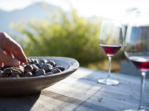 Törggelen Hand nimmt geröstete Maronen neben zwei Gläsern Rotwein auf Holztisch