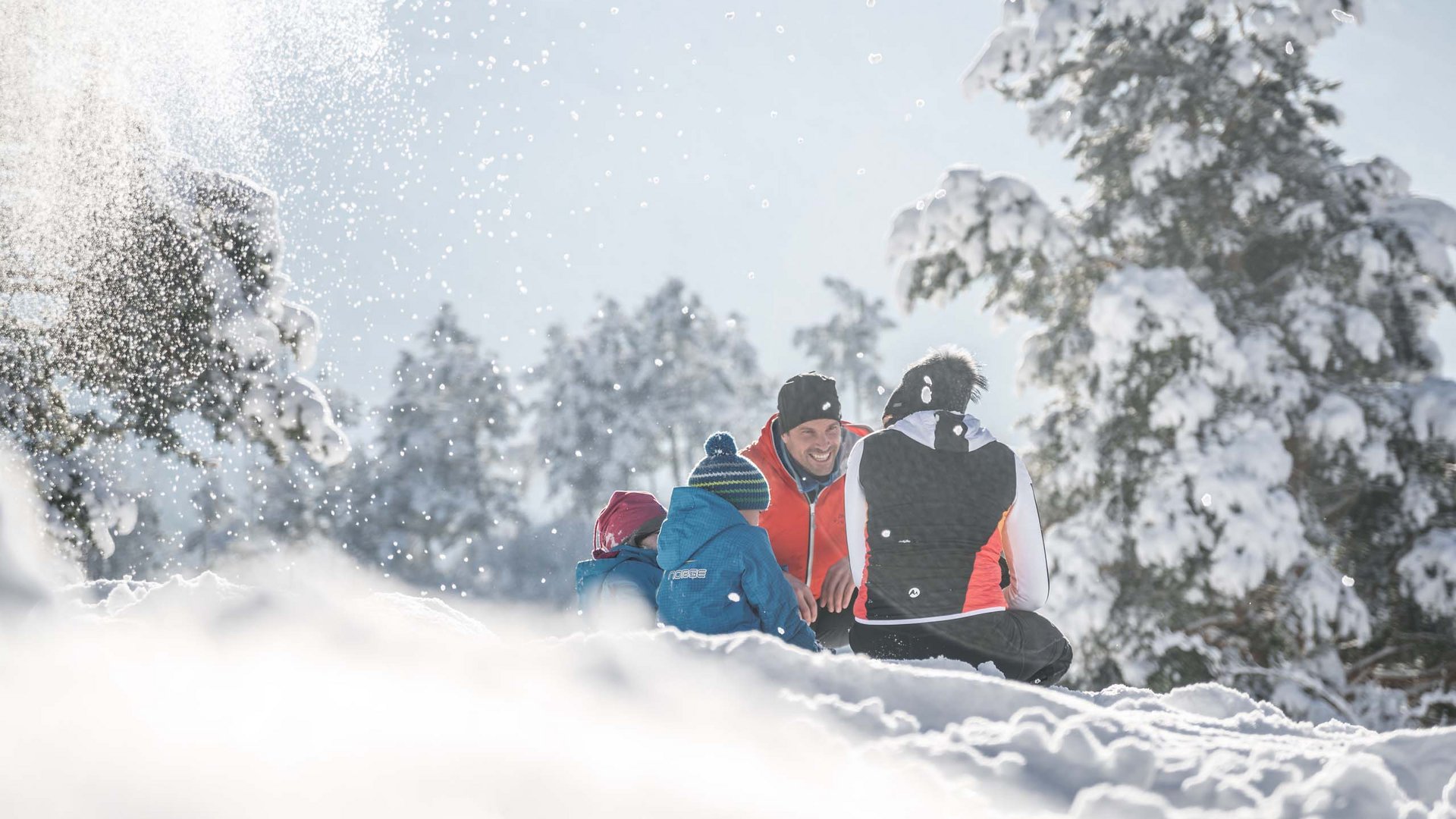 Holiday in Natz-Schabs? Kessler’s Mountain Lodge! Family sitting in snow in snowy forest on a sunny winter day