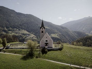 Holiday with a dog in South Tyrol: Kessler’s! Church with cemetery in front of forested mountains and blue sky