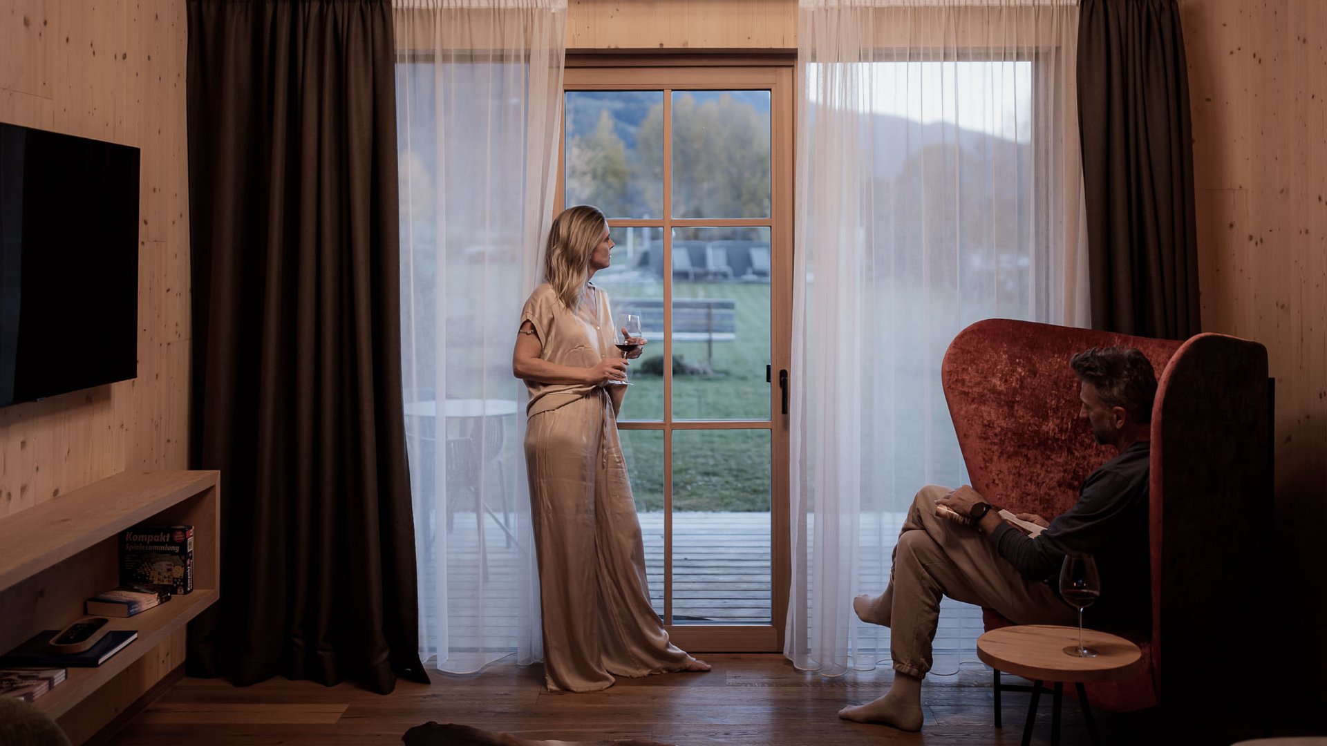 Appartamenti in Alto Adige: fuori dal comune Coppia in soggiorno con vino, donna guarda fuori dal portone verso il giardino