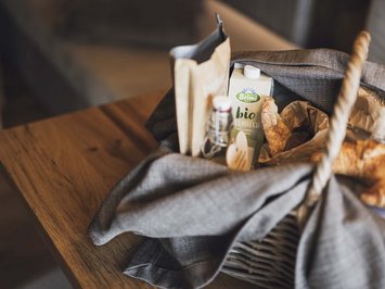 Bontà locali e di stagione al Klessler’s Cesto della spesa con latte biologico, pane e croissant su tavolo di legno