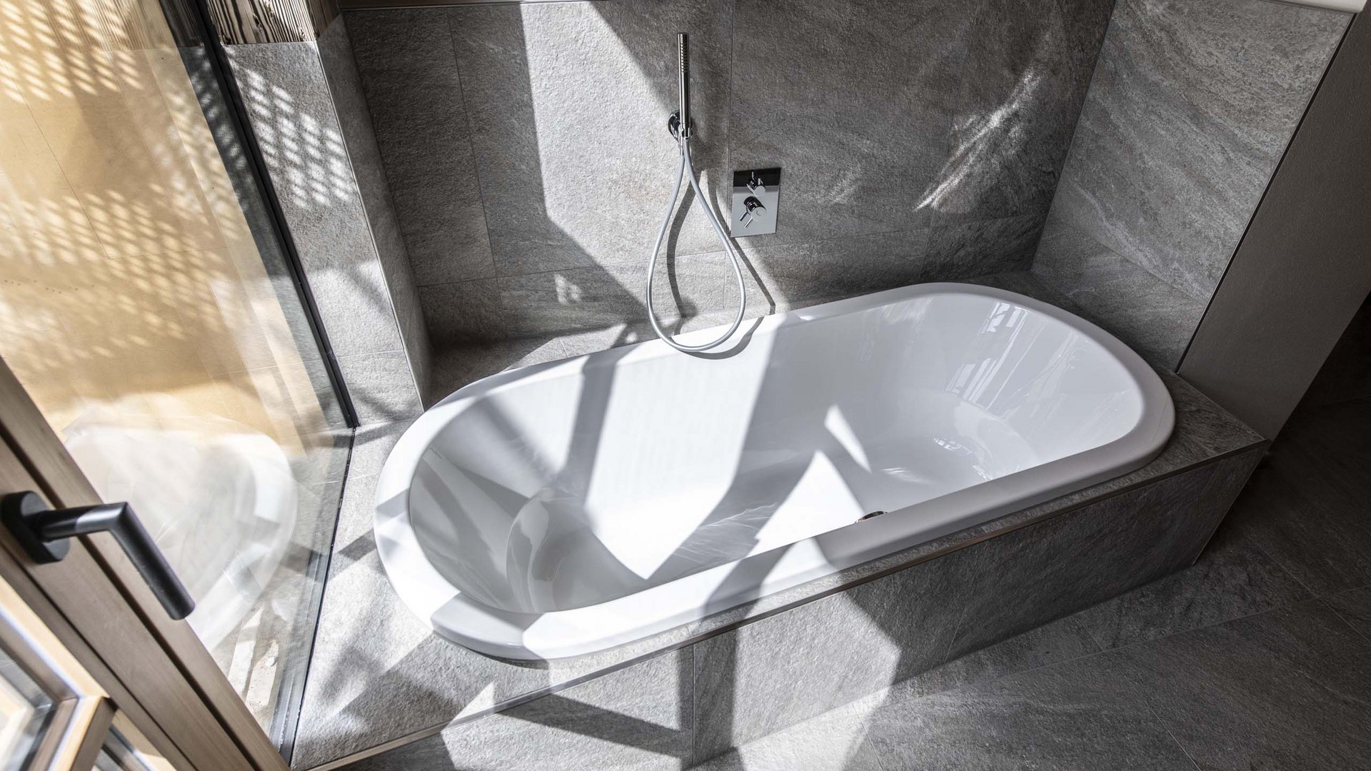 Chalet with a sauna and so much more: Kessler’s Modern bathtub with gray tiles and sunlight shadows