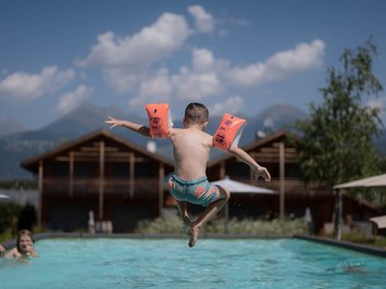 Für Familien Kind mit Schwimmflügeln springt in einen Außenpool vor Berghütten