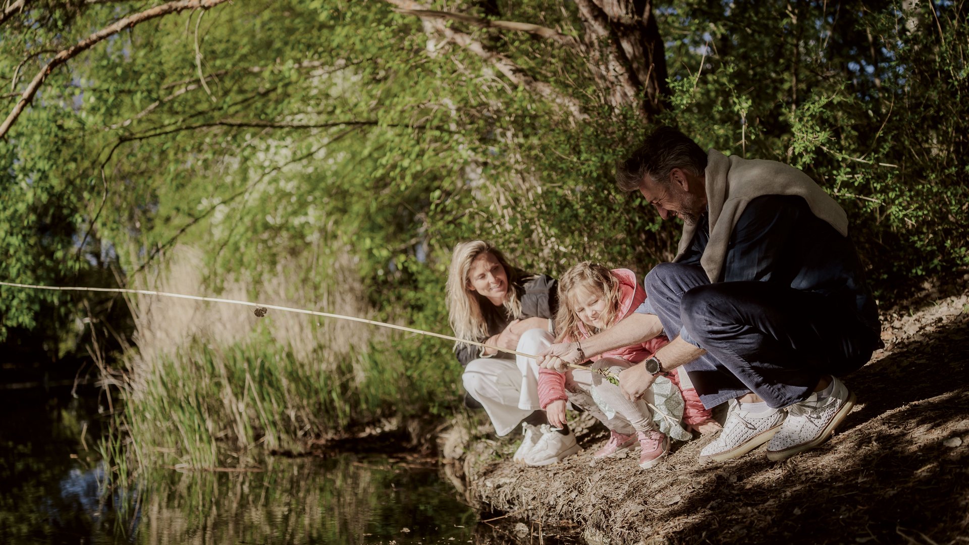 Für Familien Famiglia con bambino che pesca vicino a un fiume sotto alberi verdi